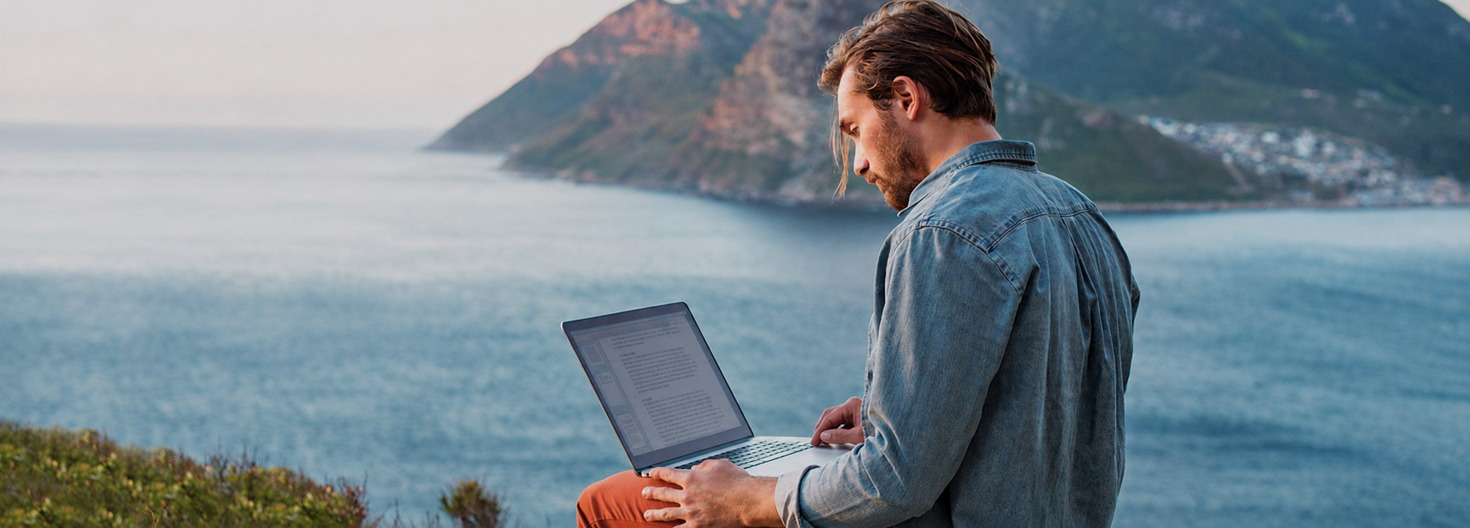 Person arbeitet an einem Laptop mit malerischem Küstenblick — Bitdefender Central Einrichtungsanleitung